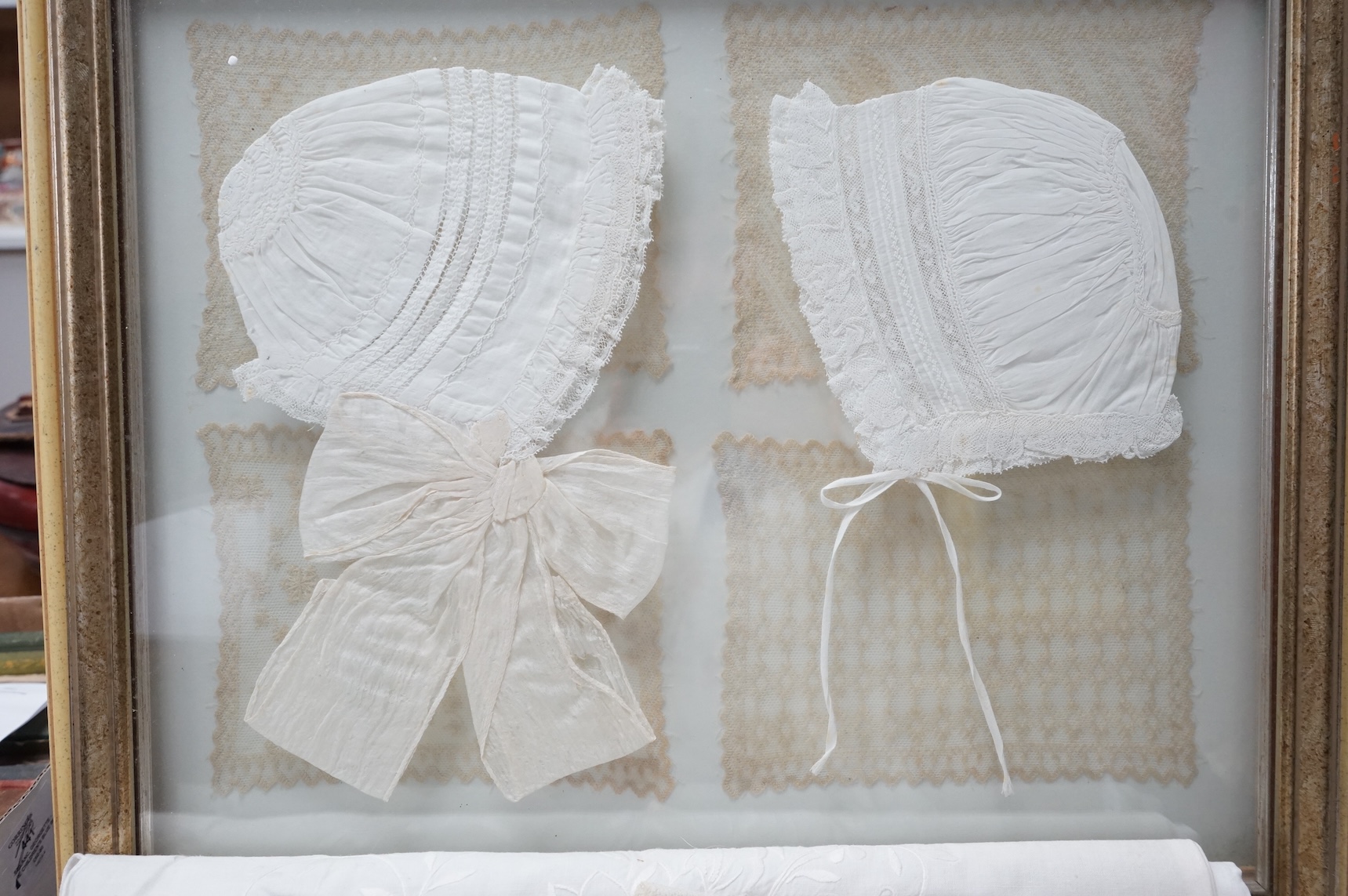A collection of lace and textiles comprising a large cutwork tablecloth, a lace cloth, framed baby bonnets and 8 lace mats (framed)